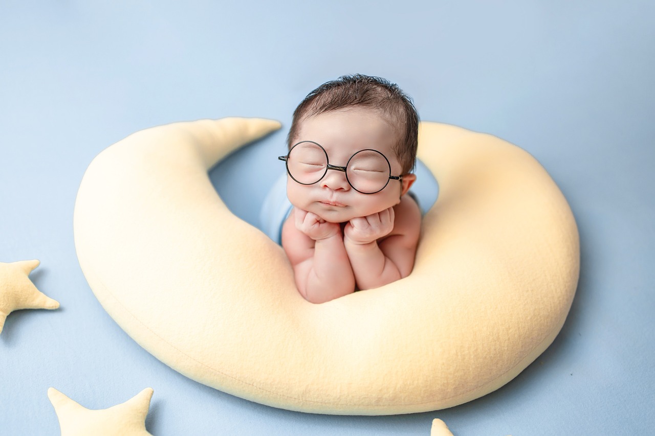image d un bébé en shooting avec des lunettes poser sur une peluche lune
