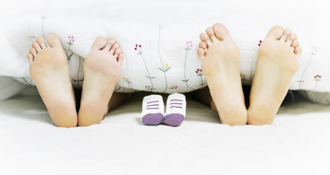 deux paires de pieds en bout de lit, 2 adultes et une paire de chausson bébé